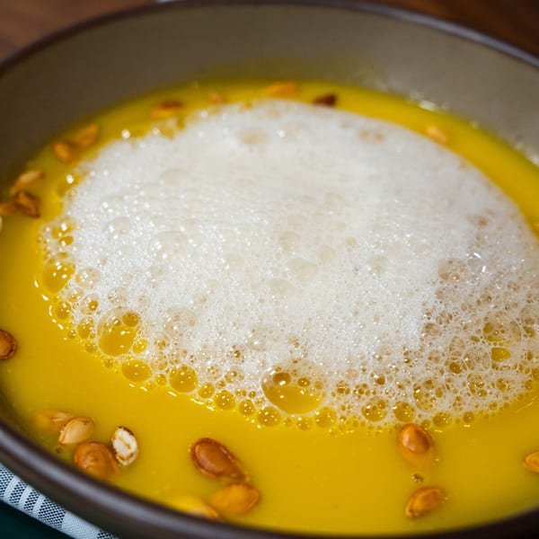Close-up of Ember's pumpkin soup with foam and pumpkin seeds in a brown bowl.