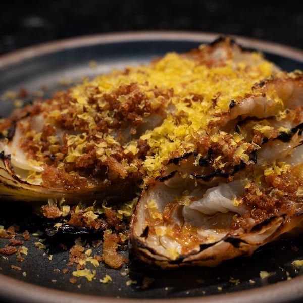 Two halves of roasted cabbage topped with golden breadcrumbs and bright yellow lemon zest.