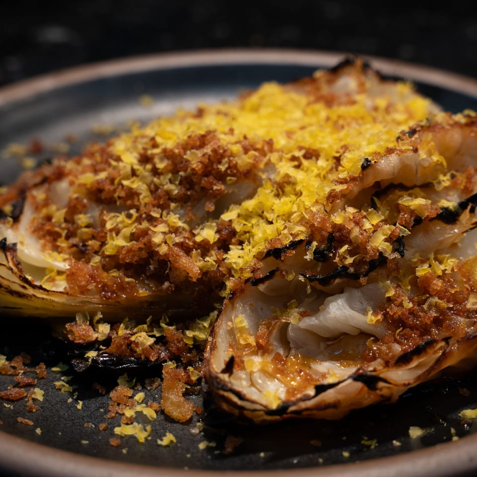 Two halves of roasted cabbage topped with golden breadcrumbs and bright yellow lemon zest.