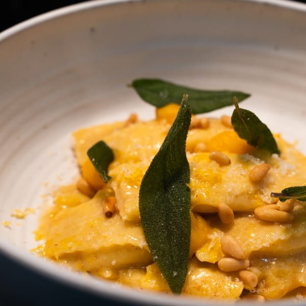 Close-up of Ember's butternut squash ravioli with sage, pine nuts, and parmesan in a white bowl.