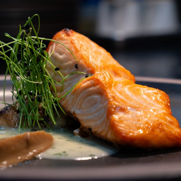 Pan-seared salmon fillet with green chives, mushrooms, and two sauces on a dark plate.