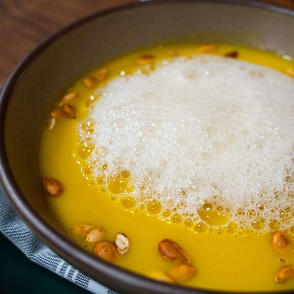 Close-up of Ember's creamy pumpkin soup with foam and pumpkin seeds in a brown bowl.