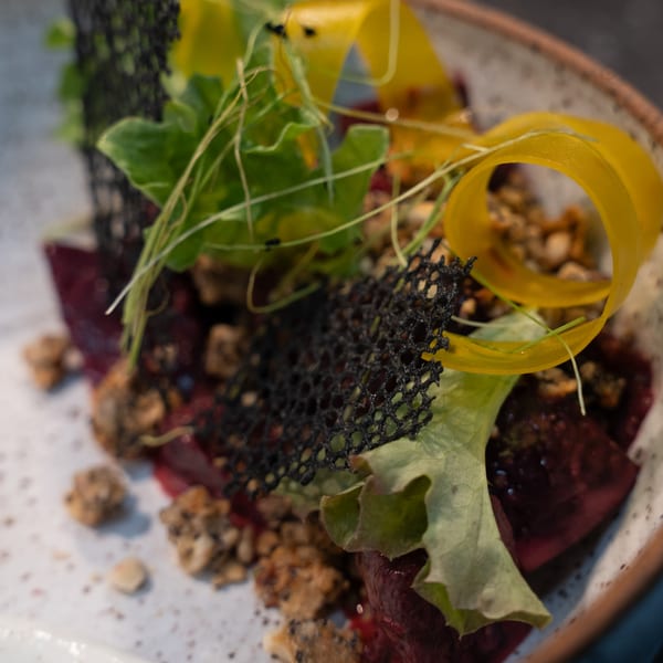 Ember's beet salad with greens, nuts, and delicate black and yellow garnishes in a rustic bowl.